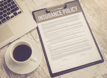 insurance policy page on a clipboard next to a cup of coffee and a laptop