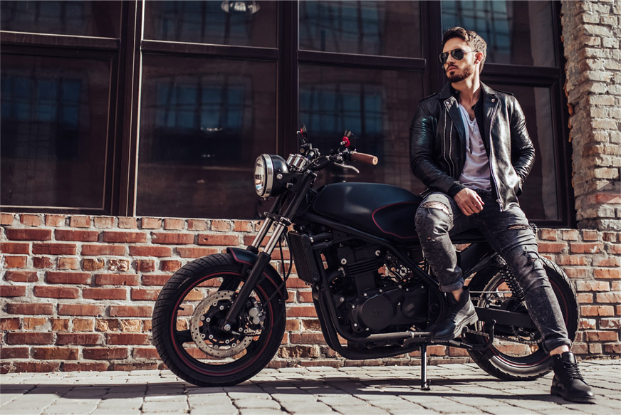 Man leaning against his motorcycle that is parked in front of a brick building
